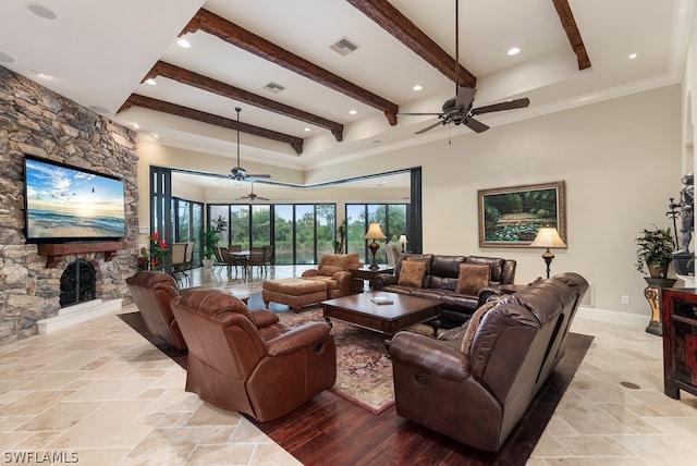 living room with crown molding, a stone fireplace, beam ceiling, light hardwood / wood-style floors, and ceiling fan