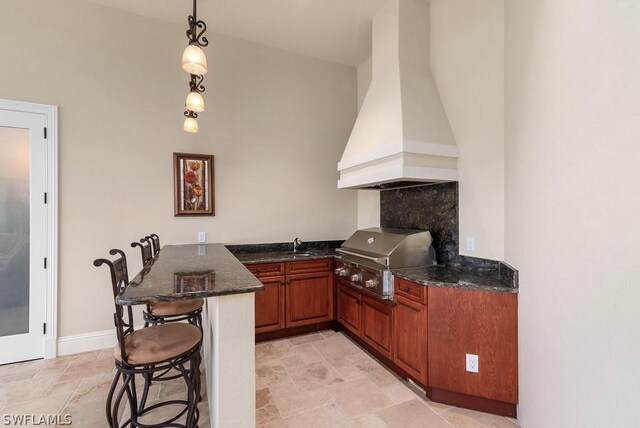 20180 Riverbrooke Run, Estero, FL 33928 - kitchen featuring custom range hood, a peninsula, stone tile floors, a breakfast bar, and dark stone counters