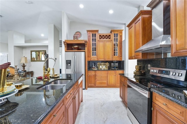 kitchen with appliances with stainless steel finishes, glass insert cabinets, a sink, wall chimney range hood, and dark stone countertops