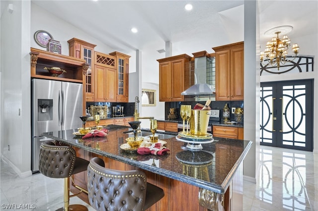 kitchen featuring dark stone counters, decorative backsplash, a center island with sink, and wall chimney range hood