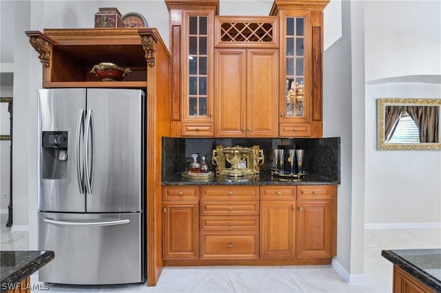 kitchen featuring stainless steel fridge, glass insert cabinets, dark stone countertops, marble finish floor, and backsplash