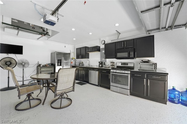 kitchen featuring dark countertops, appliances with stainless steel finishes, dark cabinets, light speckled floor, and a sink