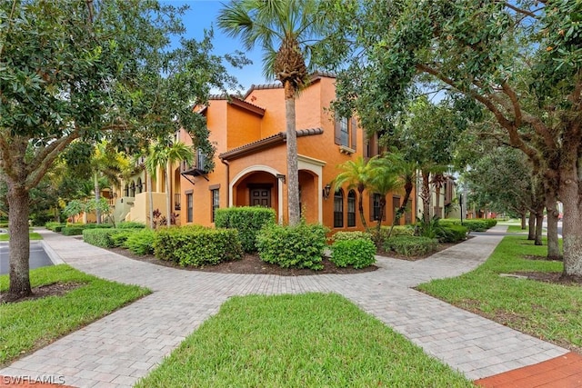 mediterranean / spanish home featuring a tiled roof, a front yard, and stucco siding