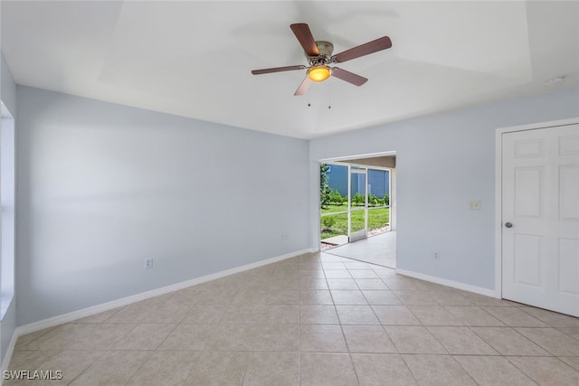 tiled empty room with ceiling fan and a raised ceiling