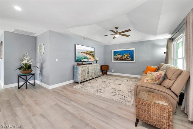 living room featuring visible vents, baseboards, a raised ceiling, ceiling fan, and light wood-style floors