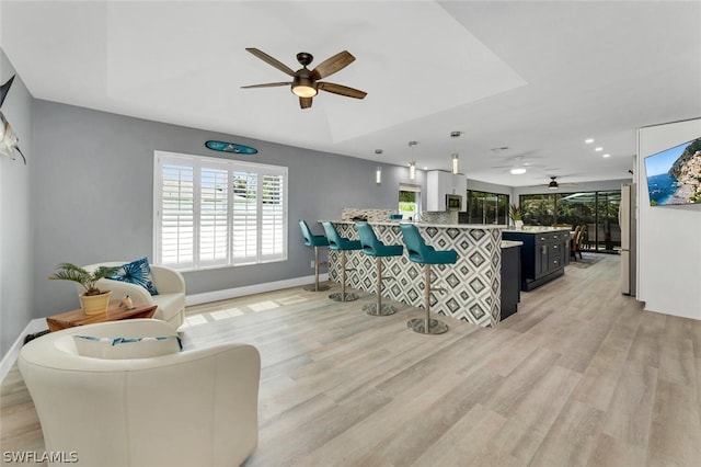 living area with baseboards, a raised ceiling, a ceiling fan, and light wood-style floors