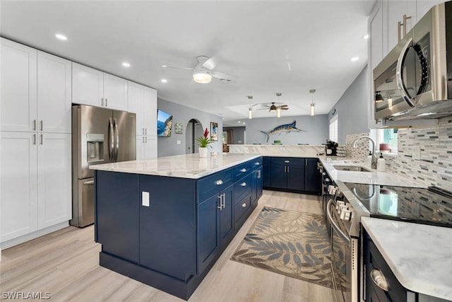 kitchen with white cabinets, a kitchen island, appliances with stainless steel finishes, blue cabinets, and a sink