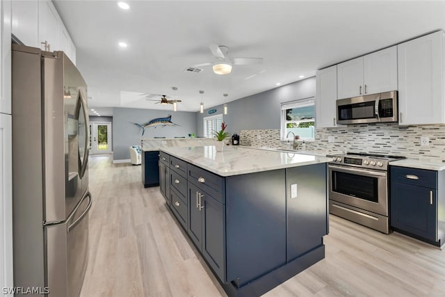 kitchen featuring stainless steel appliances, a kitchen island, white cabinetry, light wood-style floors, and backsplash