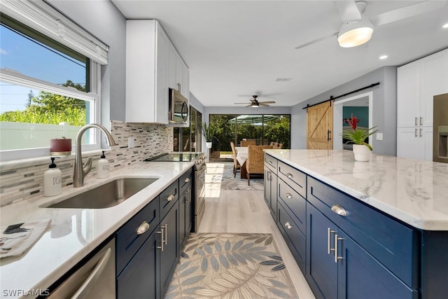 kitchen featuring stainless steel appliances, a barn door, white cabinets, and a sink