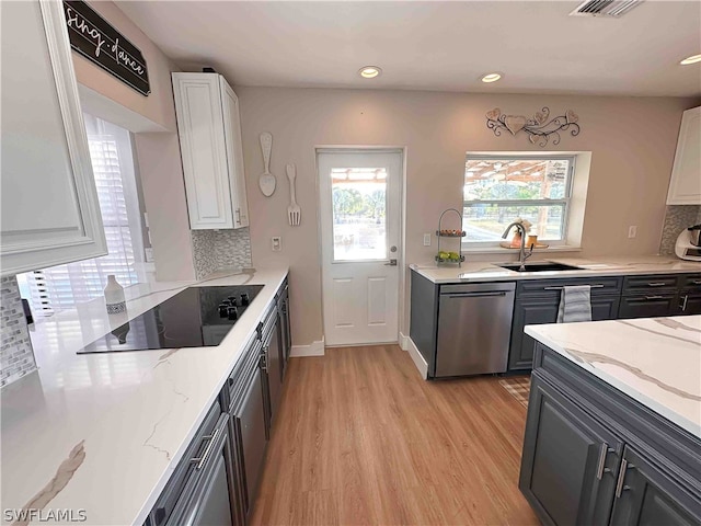 kitchen featuring black electric cooktop, light wood-type flooring, stainless steel dishwasher, tasteful backsplash, and white cabinetry