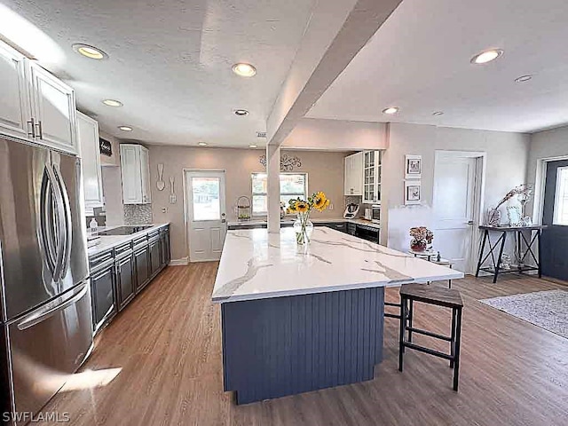 kitchen with hardwood / wood-style floors, white cabinets, a center island, light stone counters, and stainless steel fridge