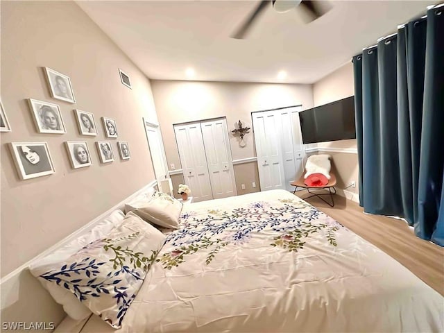 bedroom featuring visible vents, two closets, ceiling fan, vaulted ceiling, and wood finished floors