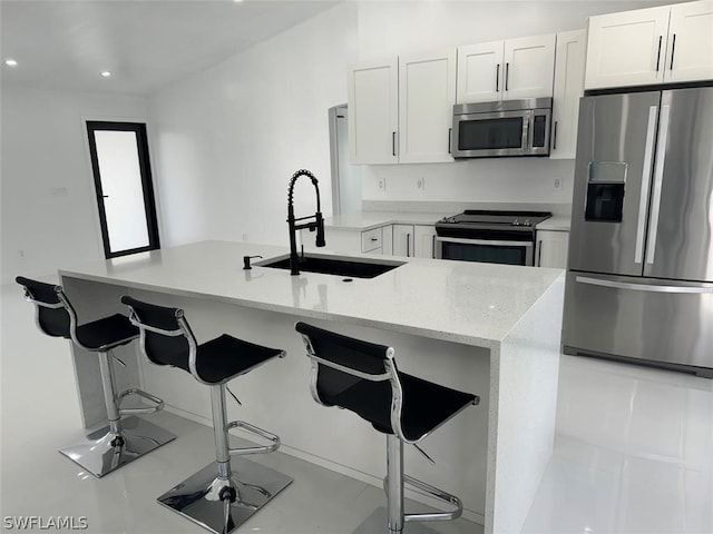 kitchen with white cabinets, sink, light stone counters, a breakfast bar area, and appliances with stainless steel finishes