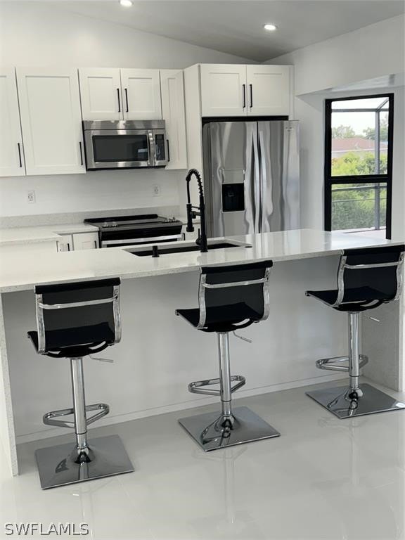 kitchen featuring a breakfast bar, white cabinets, stainless steel appliances, vaulted ceiling, and sink