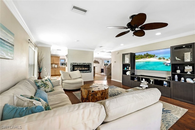 living room with a fireplace, crown molding, dark wood-type flooring, and ceiling fan