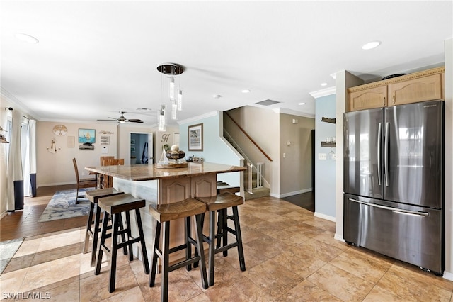 kitchen with pendant lighting, stainless steel refrigerator, a kitchen island, stone countertops, and light brown cabinetry