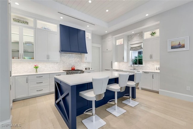 kitchen featuring a kitchen breakfast bar, white cabinets, light countertops, a center island, and wall chimney exhaust hood