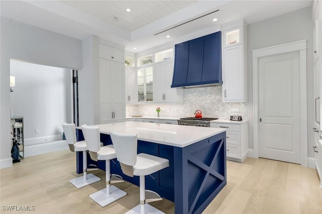 kitchen with wall chimney range hood, a kitchen bar, range, and white cabinetry