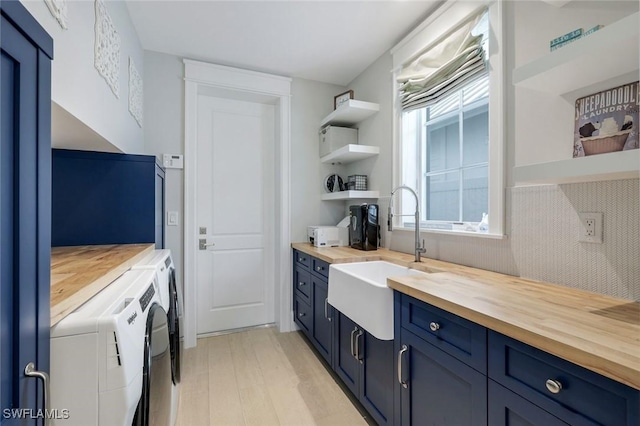 kitchen featuring butcher block countertops, a sink, blue cabinetry, open shelves, and washing machine and clothes dryer