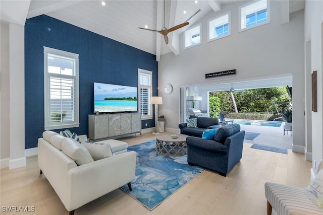 living area featuring plenty of natural light, an accent wall, beam ceiling, and wood finished floors