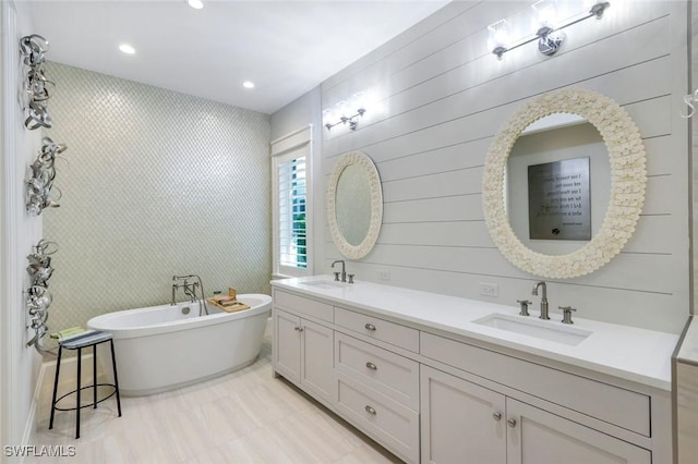 bathroom with a freestanding bath, double vanity, a sink, and recessed lighting