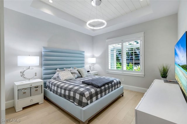 bedroom featuring a tray ceiling, light wood-type flooring, and baseboards