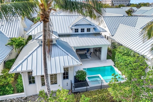 back of house with a standing seam roof, a pool with connected hot tub, metal roof, and a patio