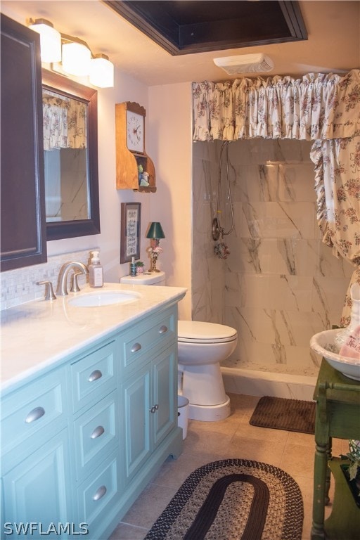 bathroom with a tile shower, vanity, a raised ceiling, tile patterned flooring, and toilet