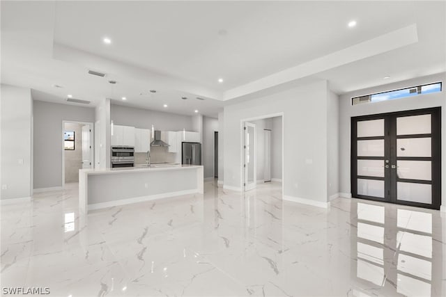 kitchen featuring stainless steel fridge with ice dispenser, an island with sink, a tray ceiling, french doors, and white cabinets