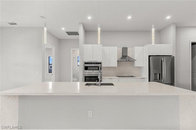 kitchen with a center island with sink, appliances with stainless steel finishes, decorative light fixtures, wall chimney exhaust hood, and white cabinets