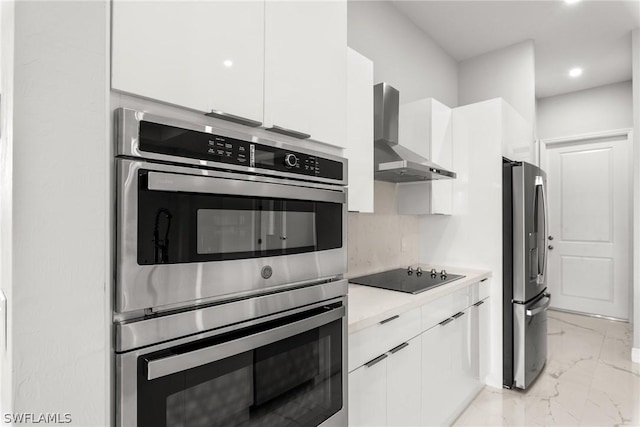 kitchen featuring appliances with stainless steel finishes, white cabinets, tasteful backsplash, and wall chimney range hood