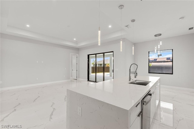 kitchen with decorative light fixtures, a center island with sink, a raised ceiling, sink, and white cabinetry