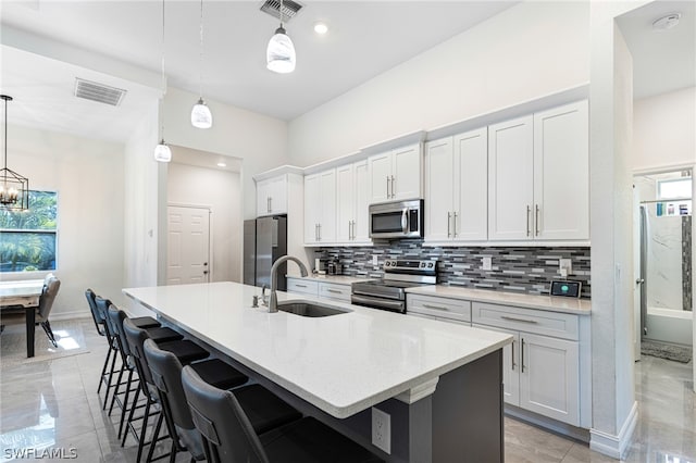 kitchen featuring a center island with sink, a kitchen bar, sink, hanging light fixtures, and stainless steel appliances