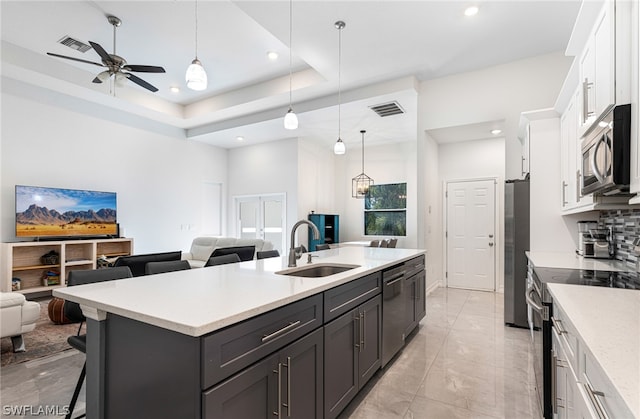 kitchen featuring a raised ceiling, sink, hanging light fixtures, appliances with stainless steel finishes, and white cabinets