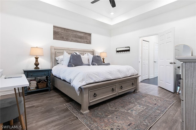 bedroom with ceiling fan, dark hardwood / wood-style floors, and a tray ceiling