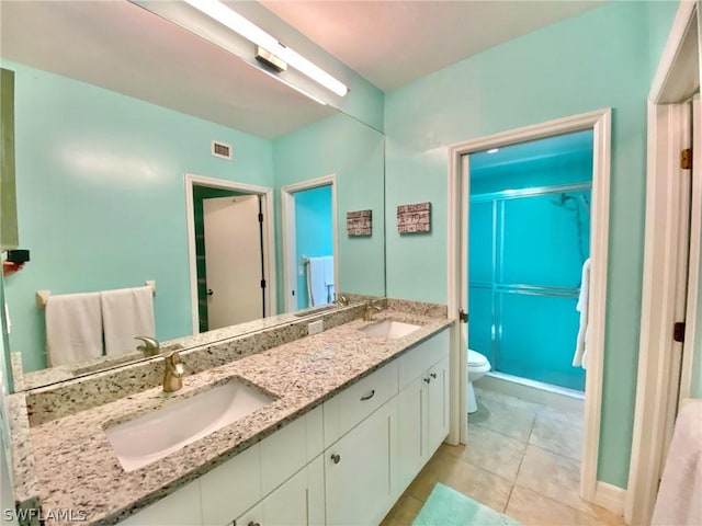 bathroom with a shower with door, vanity, tile patterned floors, and toilet