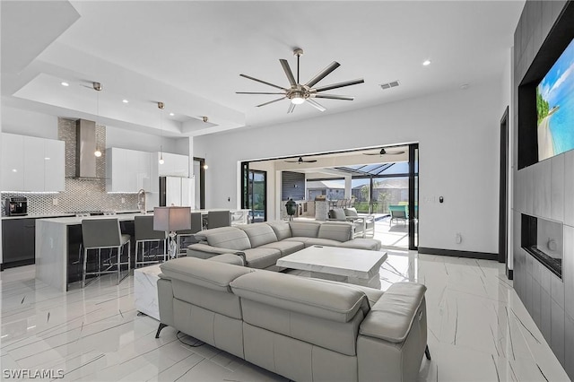 living room featuring ceiling fan, a raised ceiling, and sink