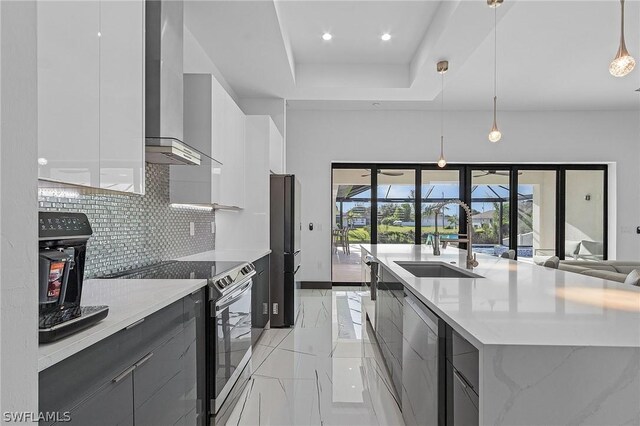 kitchen featuring wall chimney range hood, hanging light fixtures, backsplash, white cabinets, and stainless steel electric range oven