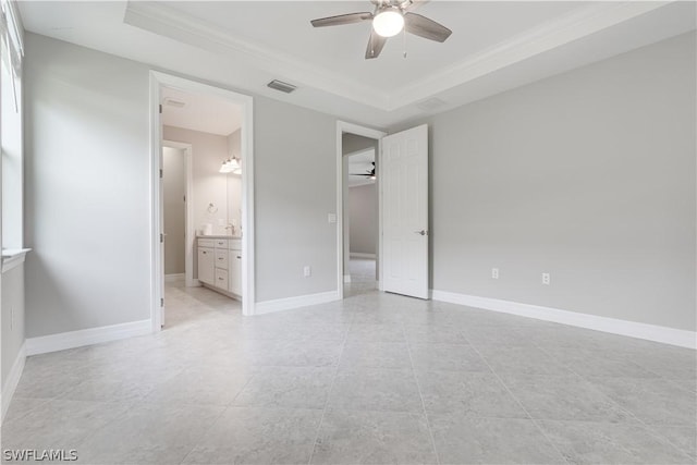 unfurnished bedroom featuring ensuite bath, ceiling fan, a tray ceiling, and ornamental molding