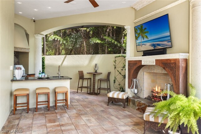 view of patio / terrace with ceiling fan, an outdoor fireplace, and exterior bar