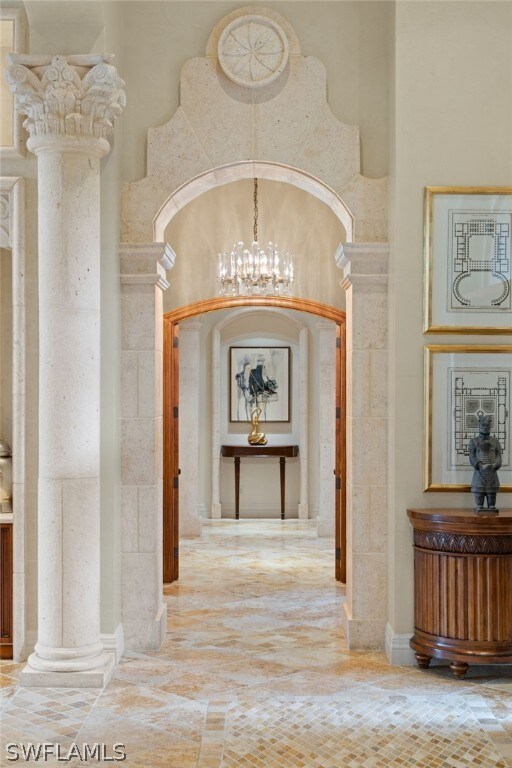 corridor featuring a notable chandelier, decorative columns, and a high ceiling