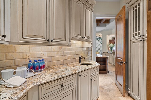 kitchen featuring tasteful backsplash, sink, light stone counters, crown molding, and cream cabinets