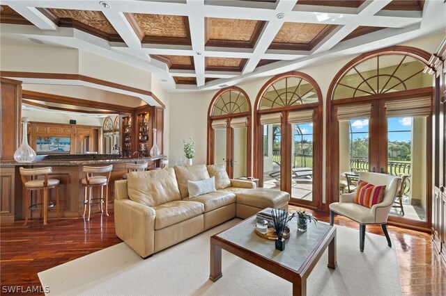 living room with a towering ceiling, beamed ceiling, dark hardwood / wood-style flooring, bar area, and french doors