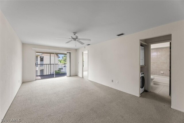 empty room featuring light colored carpet, ceiling fan, and stacked washer / drying machine