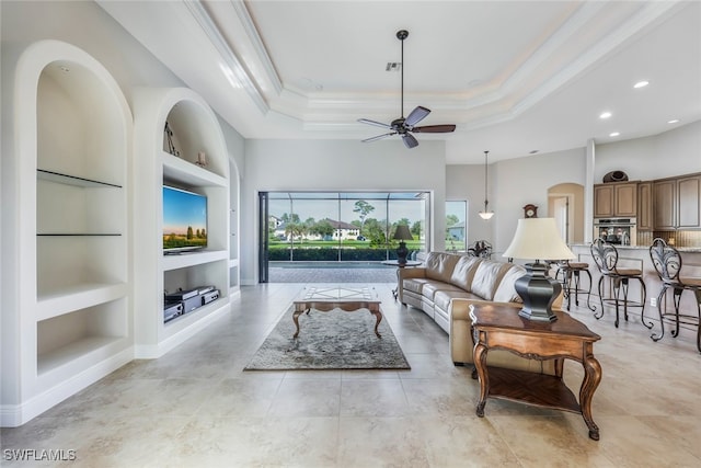 tiled living room featuring crown molding, a raised ceiling, built in features, and ceiling fan