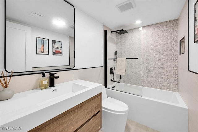 full bathroom with tile walls, tiled shower / bath, toilet, and vanity