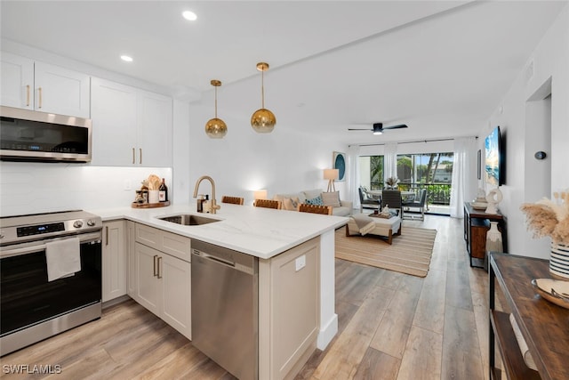 kitchen with light hardwood / wood-style flooring, stainless steel appliances, kitchen peninsula, sink, and light stone countertops