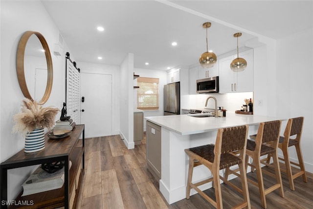 kitchen featuring a breakfast bar area, light hardwood / wood-style floors, stainless steel appliances, kitchen peninsula, and a barn door