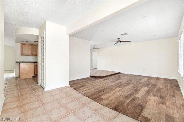 unfurnished living room featuring light tile patterned flooring, a textured ceiling, and ceiling fan