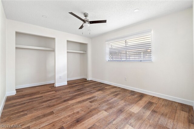 unfurnished bedroom featuring dark wood-type flooring, ceiling fan, a textured ceiling, and two closets